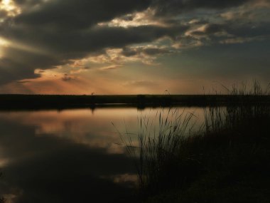 Göl, thunderclouds ve çim bir kıyısında günbatımı