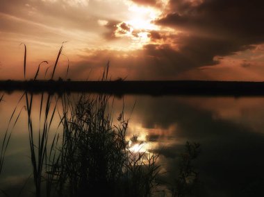Göl, thunderclouds ve çim bir kıyısında günbatımı