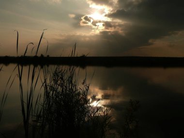 Göl, thunderclouds ve çim bir kıyısında günbatımı