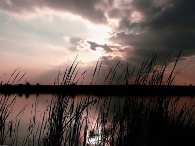Göl, thunderclouds ve çim bir kıyısında günbatımı
