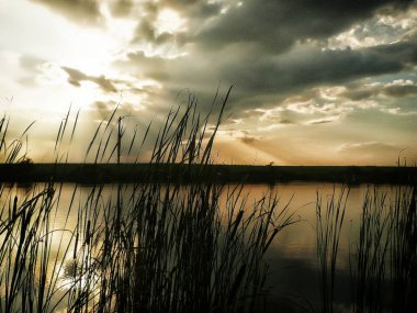 Göl, thunderclouds ve çim bir kıyısında günbatımı