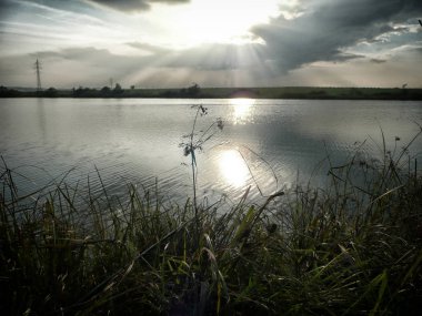 Göl, thunderclouds ve çim bir kıyısında günbatımı