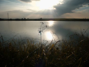 Göl, thunderclouds ve çim bir kıyısında günbatımı