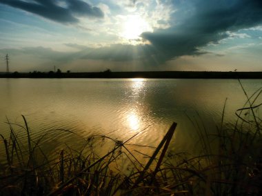 Göl, thunderclouds ve çim bir kıyısında günbatımı