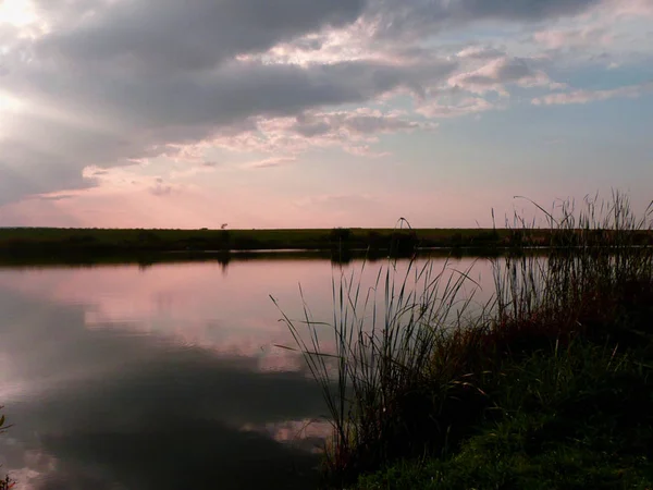 Göl, thunderclouds ve çim bir kıyısında günbatımı