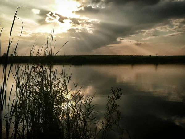 Göl, thunderclouds ve çim bir kıyısında günbatımı