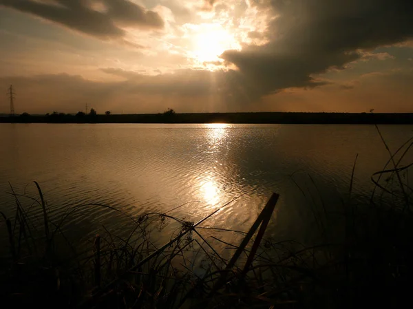 Göl, thunderclouds ve çim bir kıyısında günbatımı