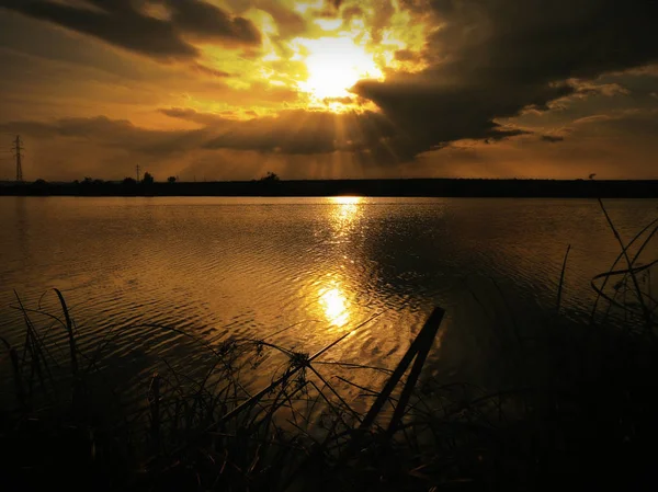 Göl, thunderclouds ve çim bir kıyısında günbatımı