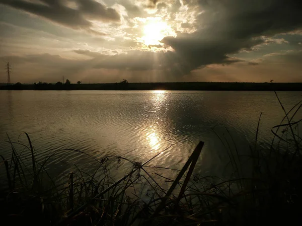 Göl, thunderclouds ve çim bir kıyısında günbatımı