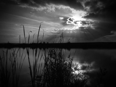 Göl, thunderclouds ve çim bir kıyısında günbatımı