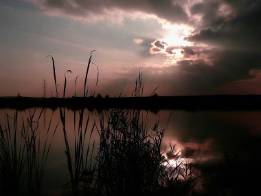 Göl, thunderclouds ve çim bir kıyısında günbatımı