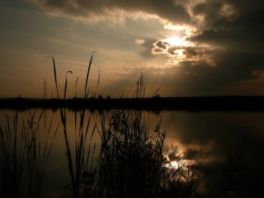 Göl, thunderclouds ve çim bir kıyısında günbatımı
