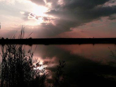 Göl, thunderclouds ve çim bir kıyısında günbatımı