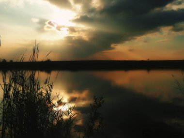 Göl, thunderclouds ve çim bir kıyısında günbatımı