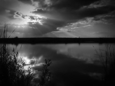 Göl, thunderclouds ve çim bir kıyısında günbatımı