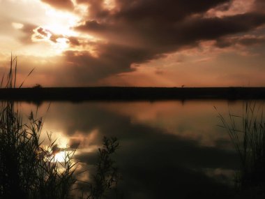 Göl, thunderclouds ve çim bir kıyısında günbatımı