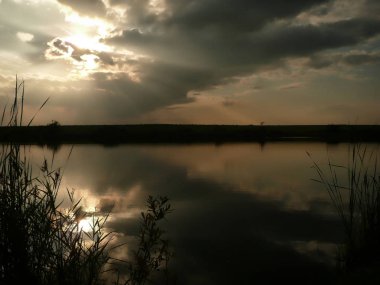 Göl, thunderclouds ve çim bir kıyısında günbatımı