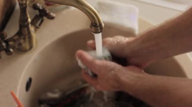 yakın çekim ellerini yıkar bir yemekler mans, su jeti tabaklar köpük ve deterjan durulama