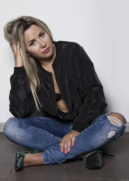 Young woman in a jeans sitting on the floor near white wall — Stock Photo, Image