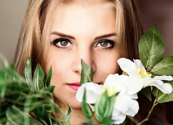 Cerrar joven rubia belleza mujer con flores sobre un fondo oscuro. maquillaje profesional — Foto de Stock