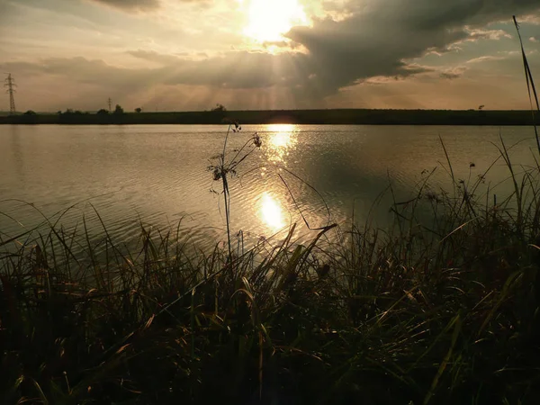 Göl, thunderclouds ve çim bir kıyısında günbatımı