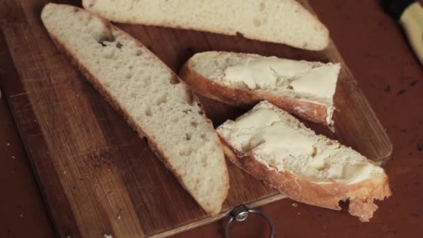 Spreading butter on a piece of wheat rural bread on a wooden board — Stock Video