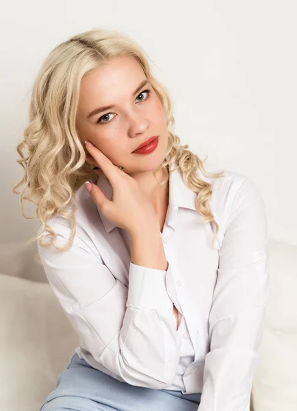 아름 다운 젊은 금발 여자는 소파에 앉아 흰색 블라우스에 — 스톡 사진