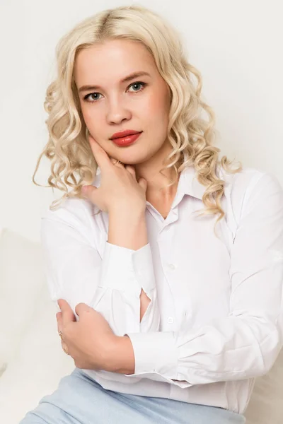 Mulher loira jovem bonita em uma blusa branca sentada em um sofá — Fotografia de Stock