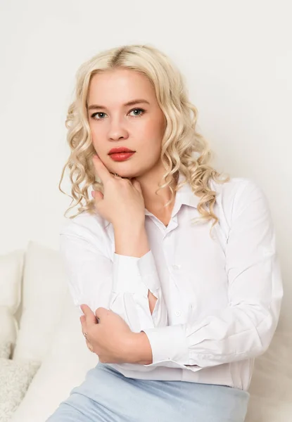 Hermosa joven rubia en una blusa blanca sentada en un sofá —  Fotos de Stock