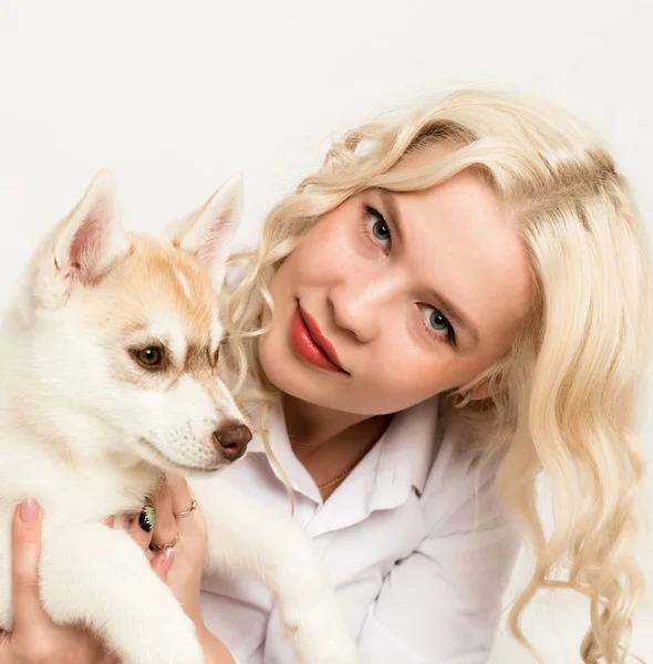 Blonde Frau mit Welpe Husky Dog auf einem weißen Sofa. Mädchen spielt mit Hund — Stockfoto