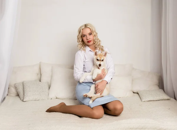 Femme blonde assise sur un canapé avec chiot chien husky. fille jouer avec un chien — Photo
