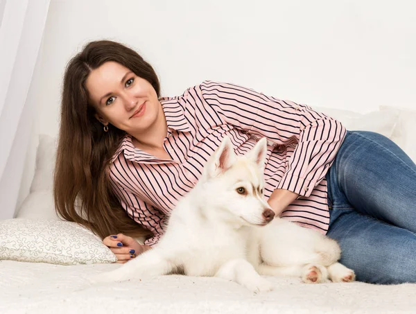 Mulher bonita feliz descansando em um sofá com seu animal de estimação. menina abraçando cachorro husky — Fotografia de Stock