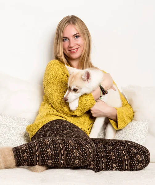 Femme blonde en pyjama et chaussettes en laine avec chiot husky repose sur un lit blanc — Photo