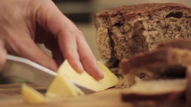 Cortar el queso en una tabla de madera. Primer plano hombre mano con cuchillo — Vídeos de Stock