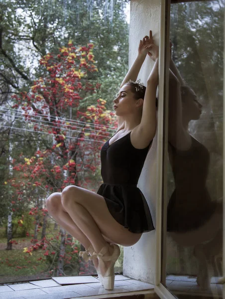 Bailarina joven en zapatos de ballet de satén posando en una ventana. sobre un fondo de paisaje otoñal — Foto de Stock