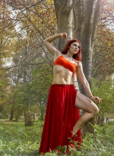 Rousse belle femme en robe rouge dansant dans une forêt d'automne . — Photo