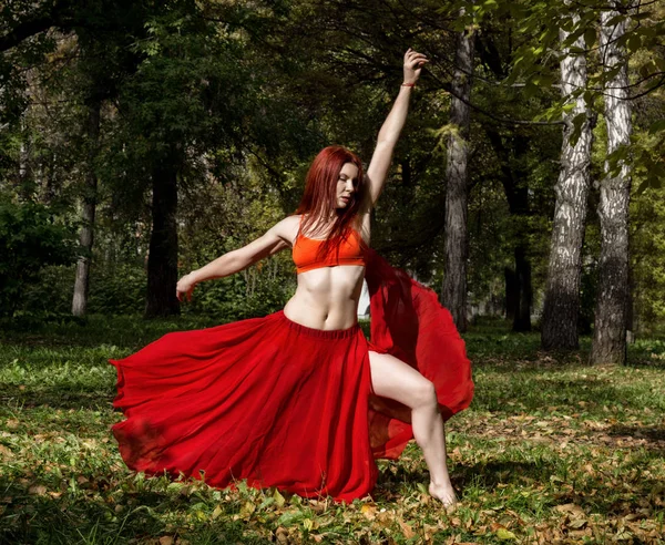 赤毛秋の森で踊る赤いドレスで美しい女性. — ストック写真