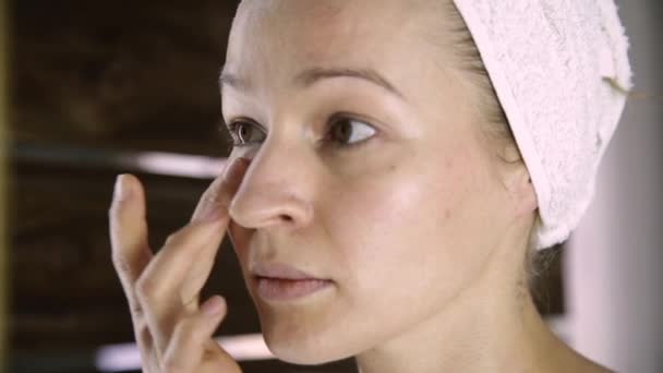 Όμορφη υγιή γυναίκα σε μια πετσέτα βάζοντας ενυδατική κρέμα στο πρόσωπο. Περιποίηση του δέρματος και Spa στο σπίτι — Αρχείο Βίντεο