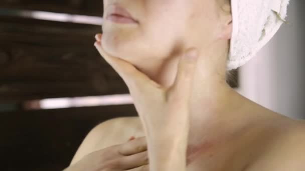 Mooie gezonde vrouw in een handdoek hydraterende crème aanbrengen op gezicht. Huid verzorging en thuis Spa — Stockvideo
