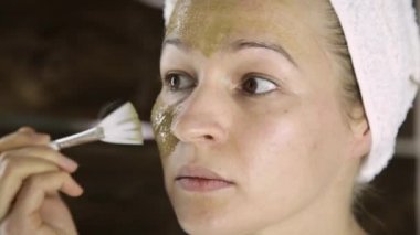 Havlu uygulanmasında güzel kadın Yeşil Kil çamur maskesi yüzüne karşı. Cilt Bakımı ve ev Spa