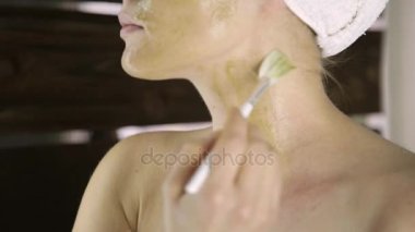 Havlu uygulanmasında güzel kadın Yeşil Kil çamur maskesi yüzüne karşı. Cilt Bakımı ve ev Spa