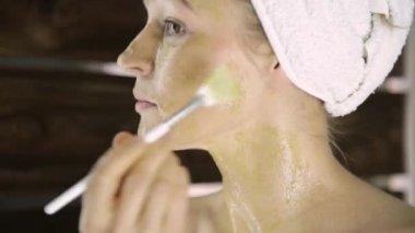 Havlu uygulanmasında güzel kadın Yeşil Kil çamur maskesi yüzüne karşı. Cilt Bakımı ve ev Spa