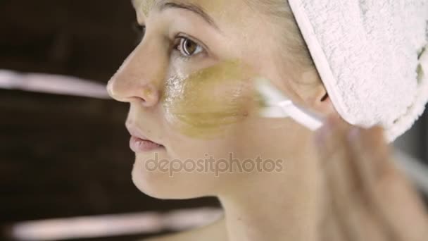 Bella donna in asciugamano applicare maschera di fango verde argilla al viso. Cura della pelle e casa Spa — Video Stock