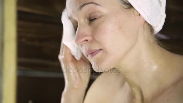 Bela mulher em toalha de limpar o rosto com uma almofada de algodão. menina lavar fora máscara de rosto . — Vídeo de Stock