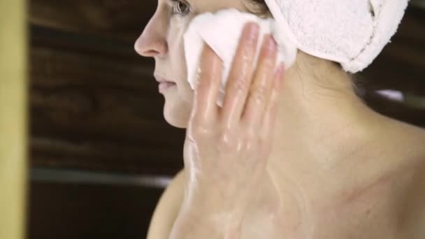 Όμορφη γυναίκα σε πετσέτα καθαρισμού το πρόσωπό της με ένα βαμβάκι. κορίτσι ξεπλύνετε μάσκα από το πρόσωπο. — Αρχείο Βίντεο