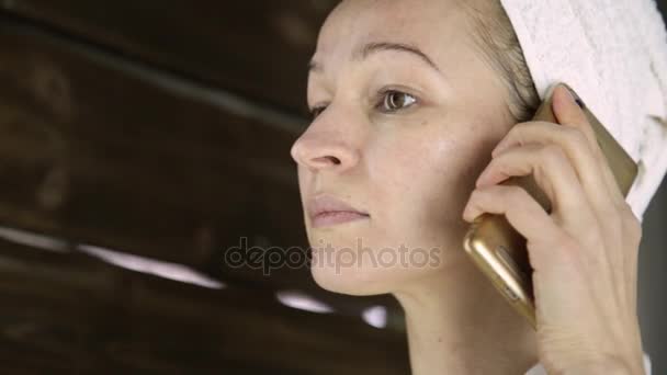 Hermosa mujer en toalla limpiando su cara con una almohadilla de algodón y hablando por teléfono — Vídeos de Stock