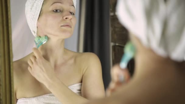 Piękna kobieta w ręcznik robi zabiegi kosmetyczne w domu. masaż twarzy z masażysta — Wideo stockowe