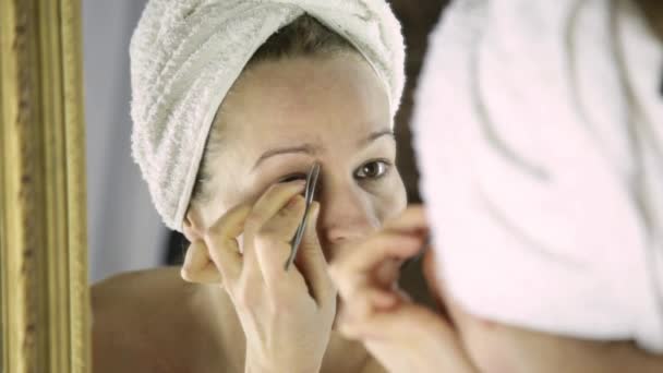 Mooie vrouw in de handdoek plukken haar wenkbrauwen. Huid verzorging en thuis Spa — Stockvideo