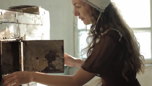 Mujer en un vestido rústico sentado al lado de la vieja estufa en una casa abandonada en ruinas — Vídeos de Stock