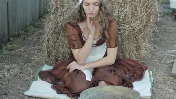 Beautiful woman in a rustic dress sits on a hay and sifts the grain — Stock Video